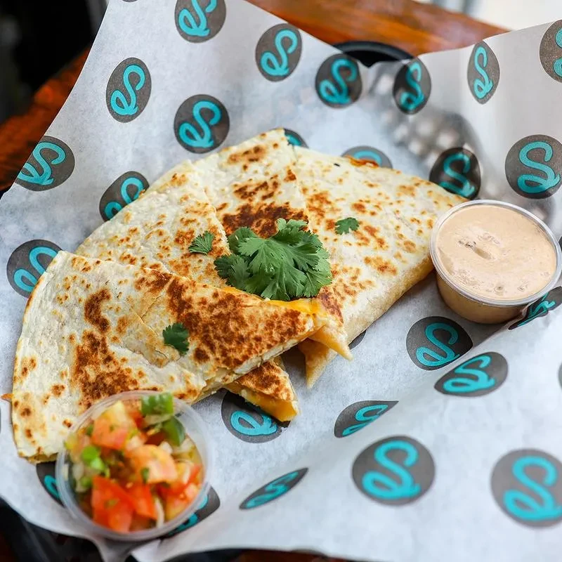 Crispy quesadilla triangles in a basket with pico de gallo and dipping sauce.