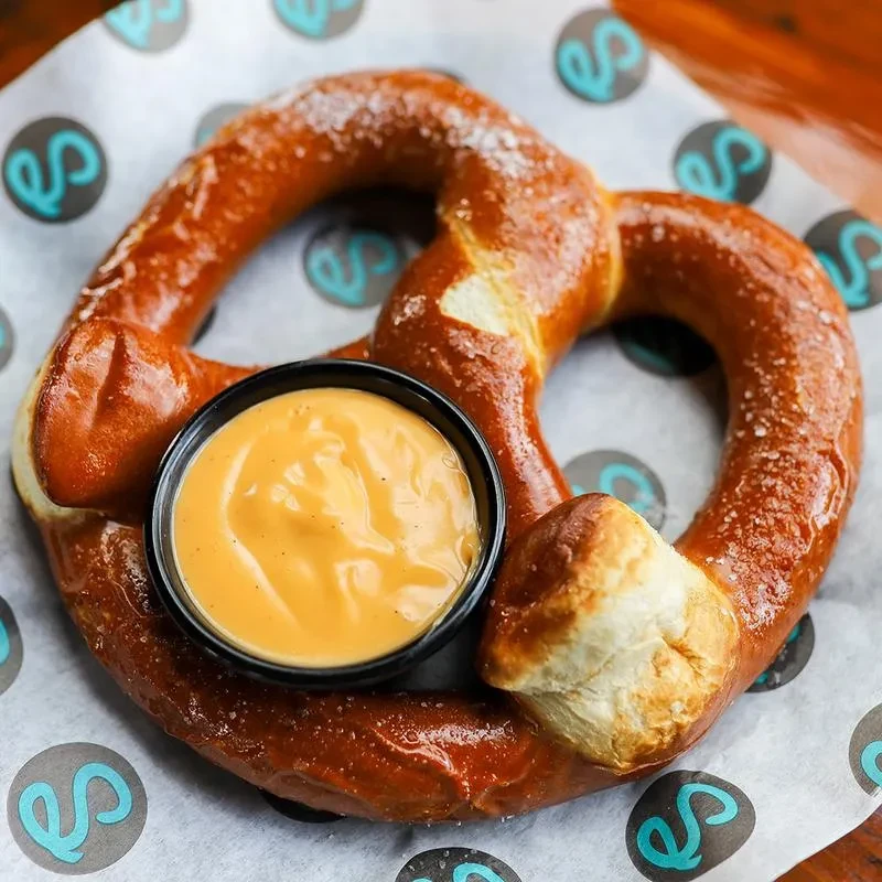 Golden-brown soft pretzel with coarse salt and orange dipping sauce.