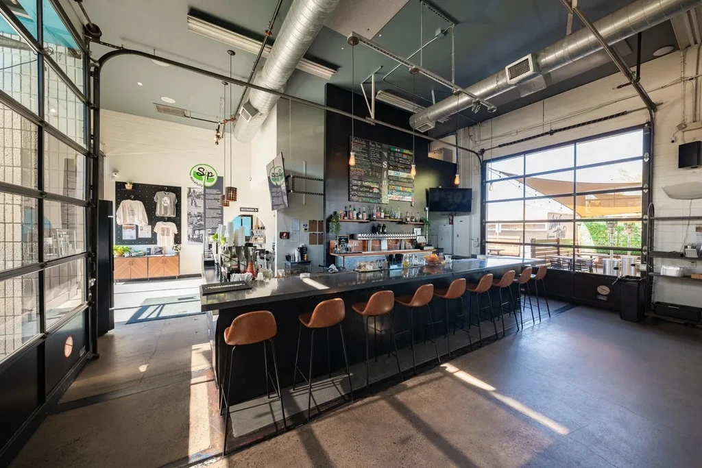 Modern industrial bar interior with long counter and garage-style doors.