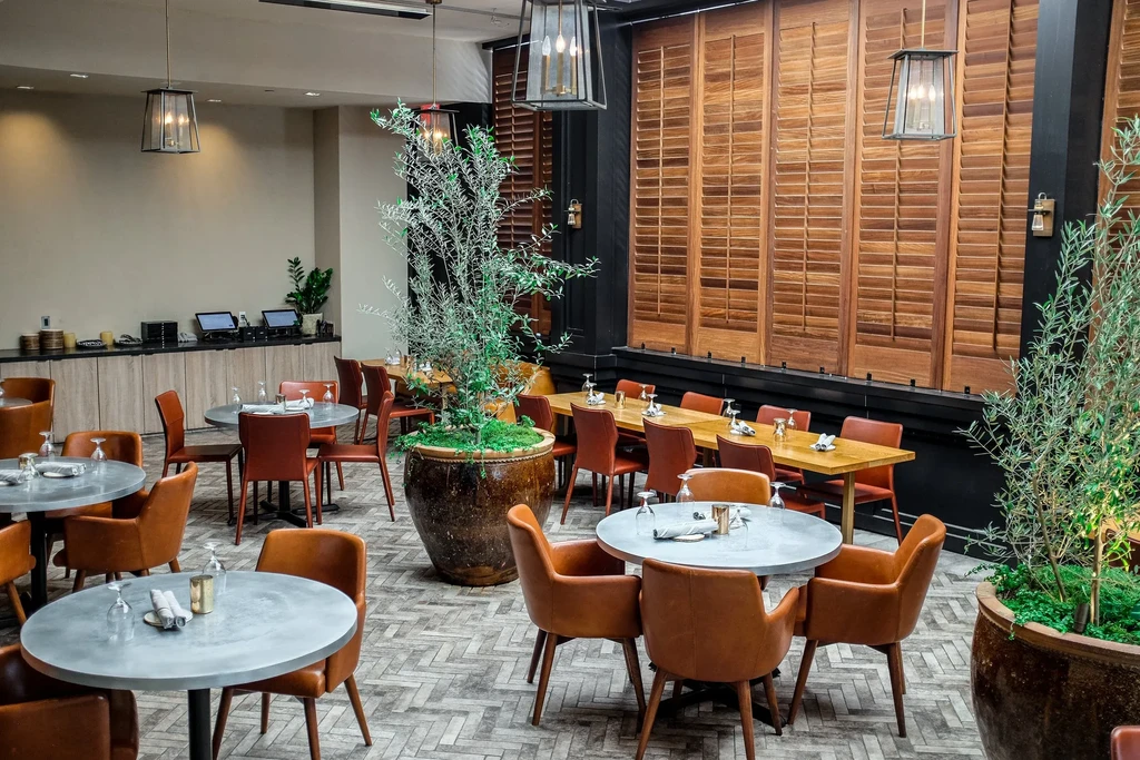 Empty, modern restaurant interior with dining tables, chairs, and potted plants.