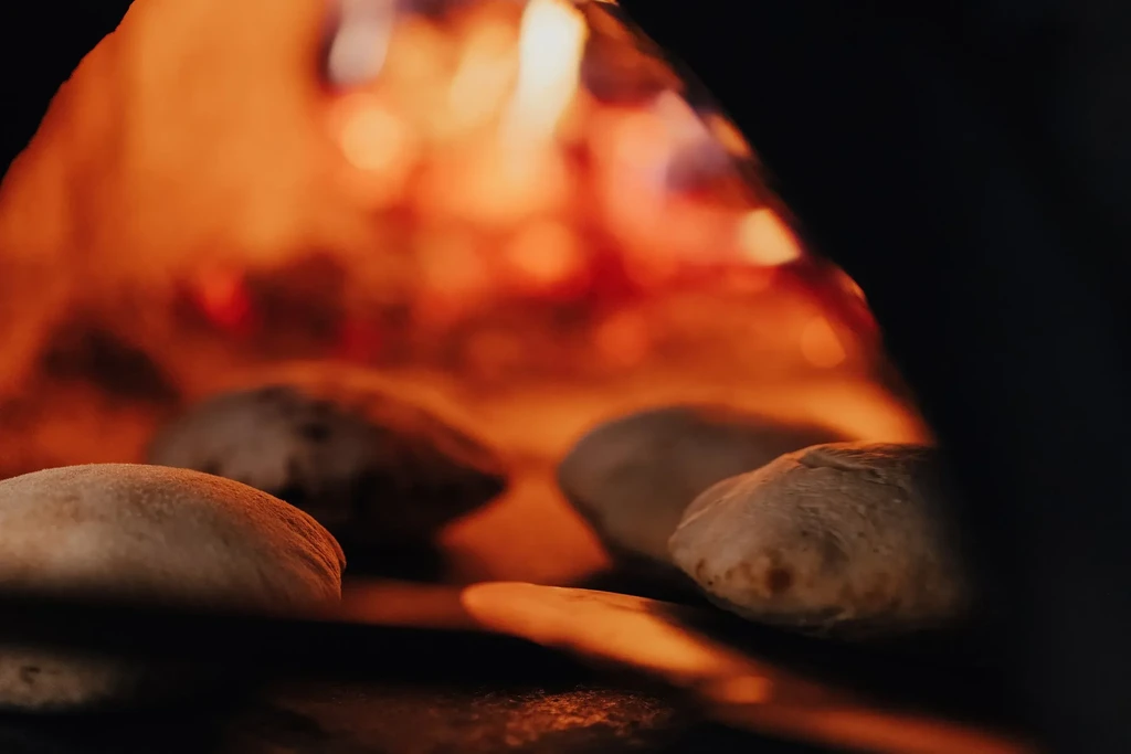 Puffy flatbread baking inside a traditional oven with flames.