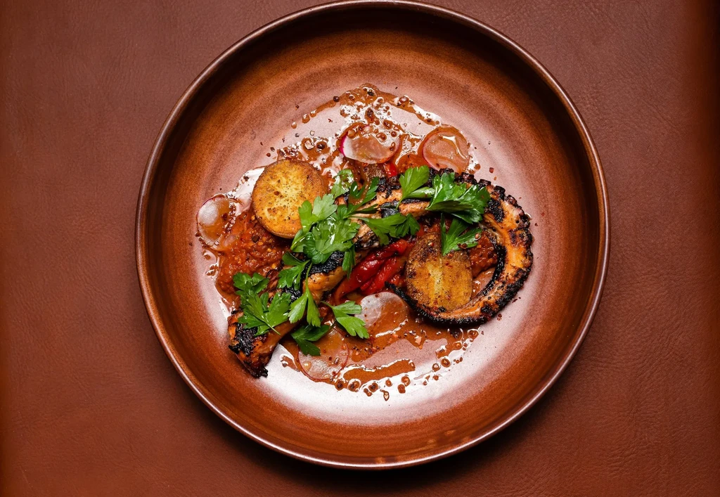 Charred grilled octopus, roasted potatoes, and parsley on a rustic plate.