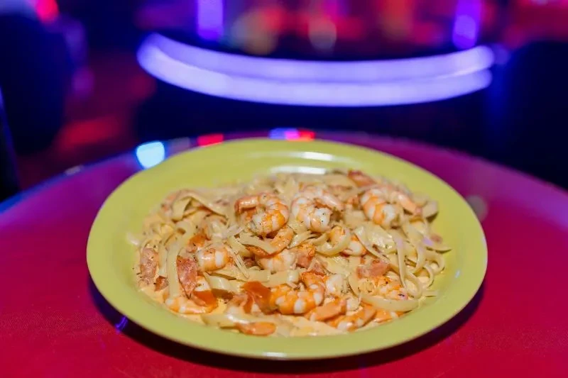 Creamy shrimp pasta on lime-green plate, colorful blurred background.