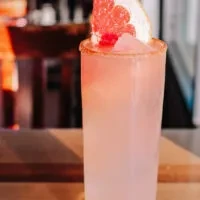 Pink cocktail with ice, grapefruit slice, red berries, and seasoned rim.