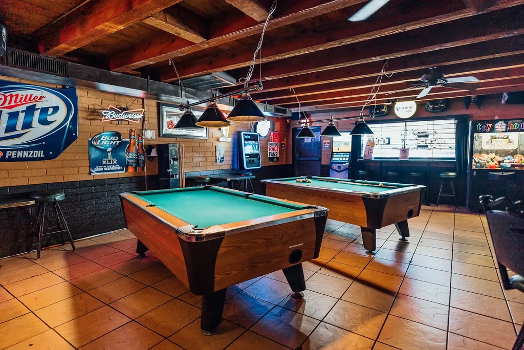 Two green felt pool tables inside a dimly lit bar.
