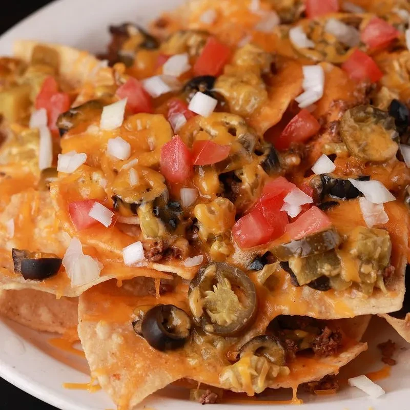 Close-up of nachos with cheese, meat, tomatoes, onions, olives, jalapeños.