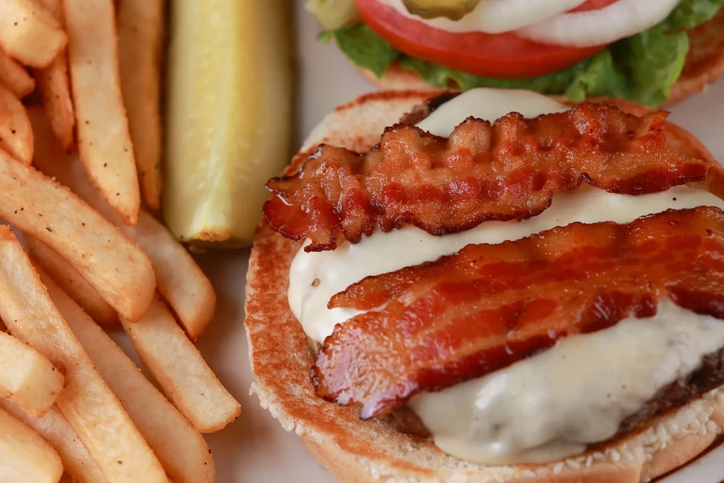Close-up of a bacon cheeseburger, golden fries, and a pickle spear.