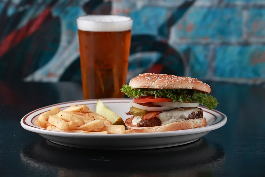 Close-up of a burger, fries, pickle spear, and beer.