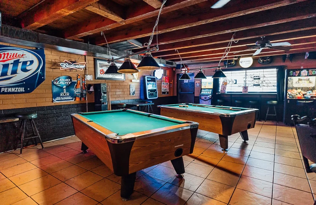Rustic bar interior with two green pool tables and branded signs.
