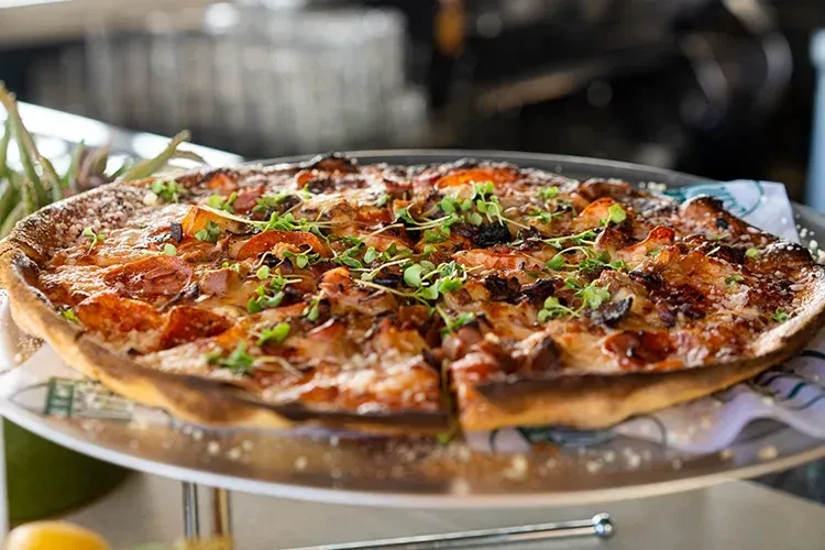 Large pizza with pepperoni, potatoes, cheese, and microgreens on a silver stand.