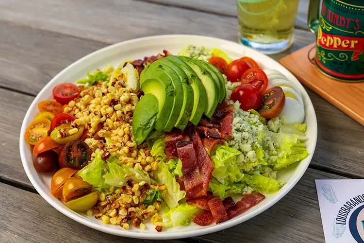 Vibrant Cobb salad with avocado, bacon, corn, tomatoes, blue cheese on wood.