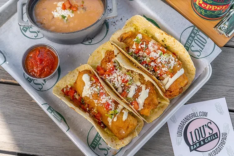 Overhead: Three fish tacos with sides on Lou's Bar & Grill tray.