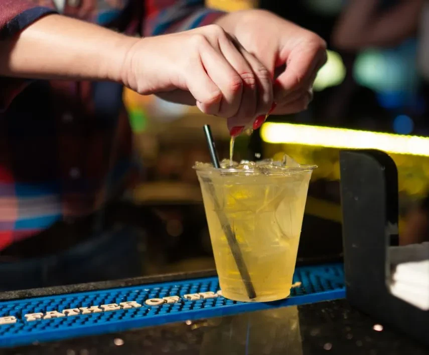 Red-nailed hands squeeze citrus into an iced drink with a black straw.
