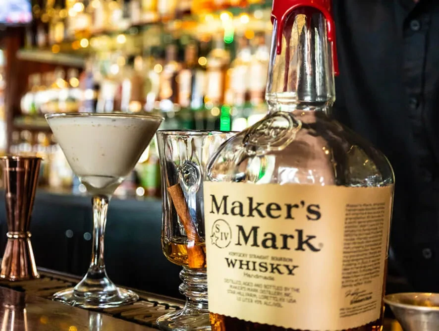 Maker's Mark bourbon bottle, cocktails, and bartender in a sophisticated bar.