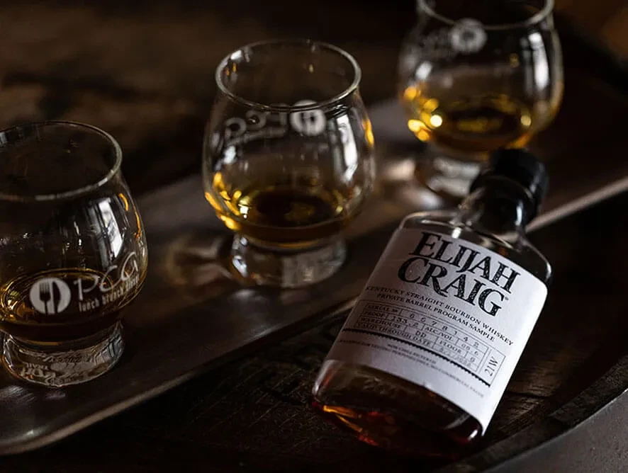Dimly lit whiskey tasting setup with Elijah Craig bottle and snifter glasses.