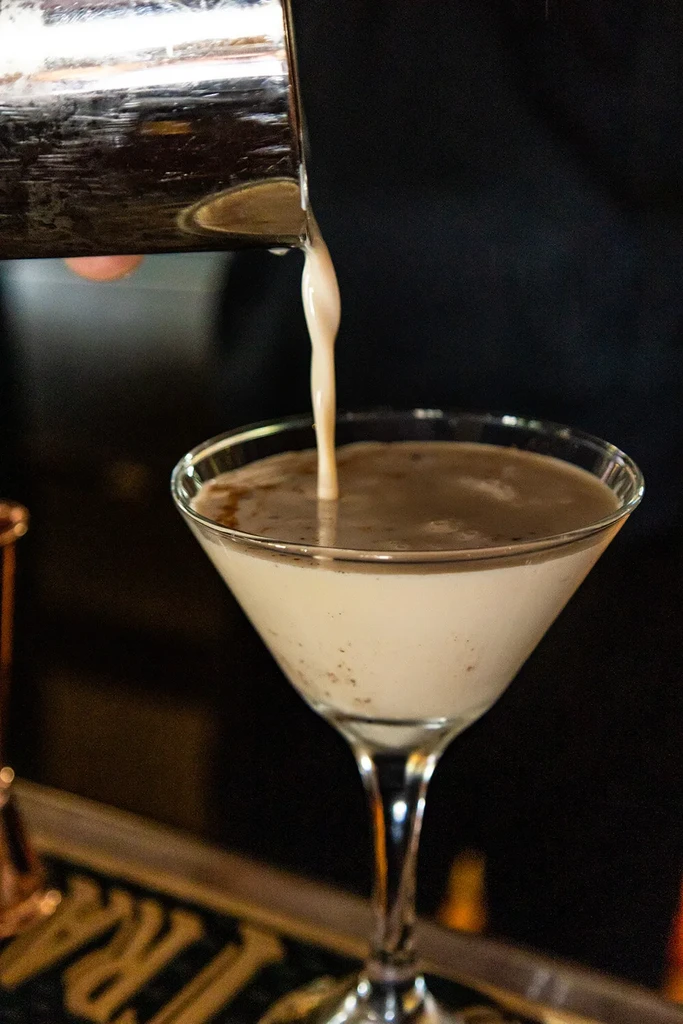 Cocktail shaker pouring a creamy, layered drink into a martini glass.