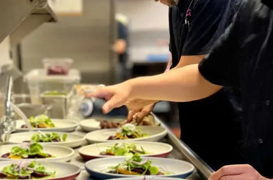 Close-up of chefs plating multiple detailed appetizers in a commercial kitchen.