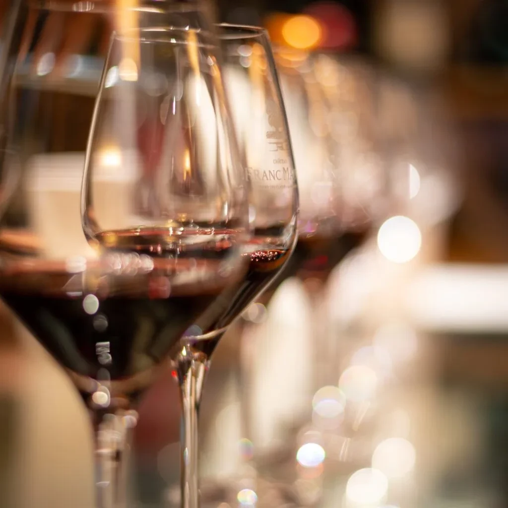 Several red wine glasses, one etched 'FRANC MAY', with a bokeh background.