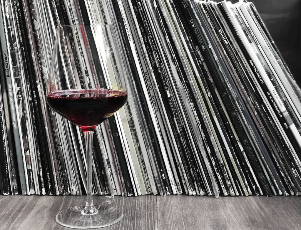 Elegant red wine glass on wood, with stacked vinyl records background.