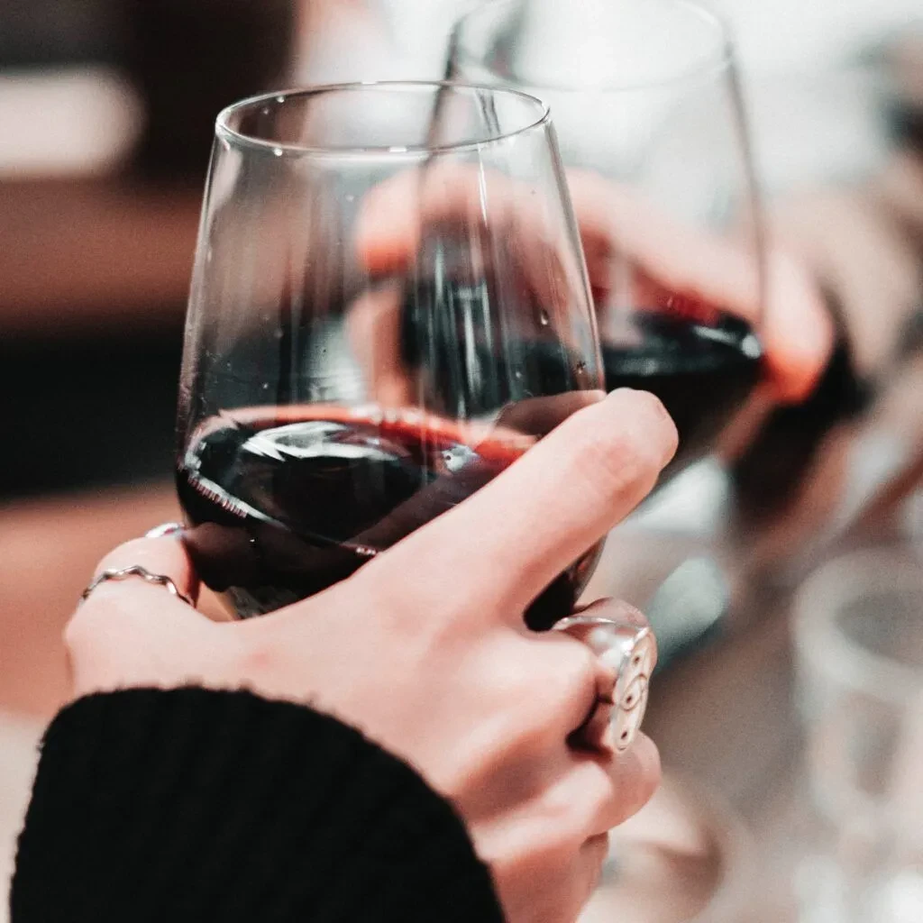 Close-up of two hands toasting with red wine glasses.
