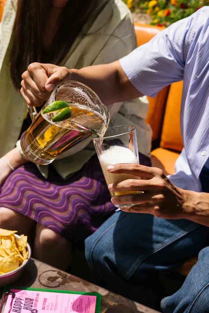 Person pours beer with lime from pitcher; chips and Happy Hour menu.