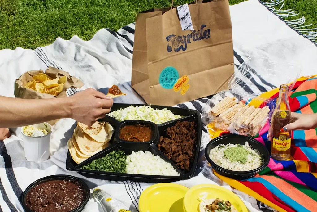 Outdoor picnic with hands sharing Mexican tacos and chips.