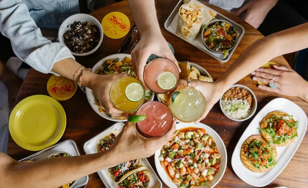 Overhead: Group toasts colorful cocktails and Mexican food.