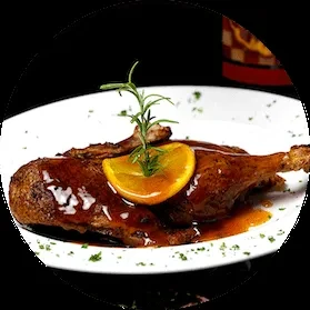 Cooked duck leg with glossy orange sauce, orange slice, and rosemary.