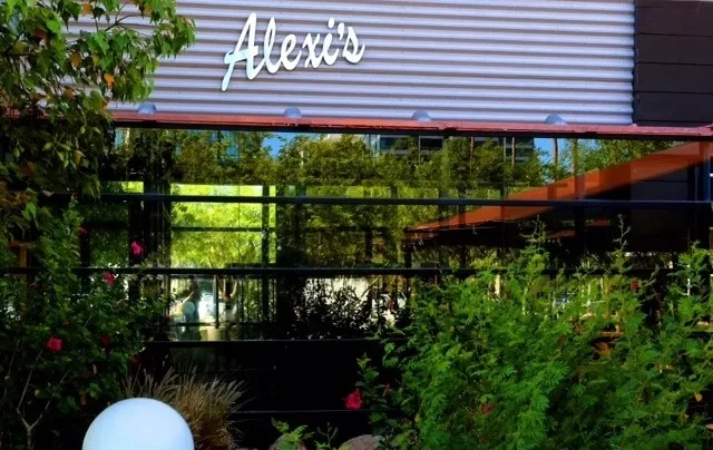 Exterior of Alexi's restaurant with reflective windows mirroring green trees.