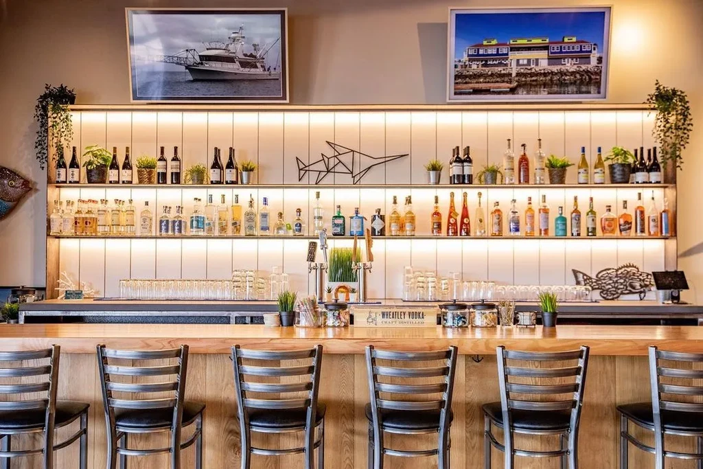 Modern bar counter with stools, illuminated liquor display, and coastal theme.