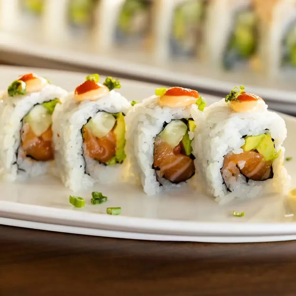 Four inside-out salmon sushi rolls with avocado, sauce, and chives.