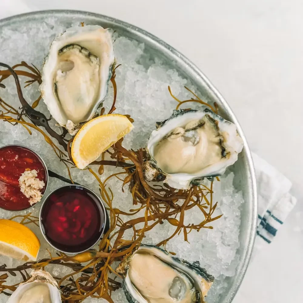 Oysters on ice with lemon, sauces, and seaweed.