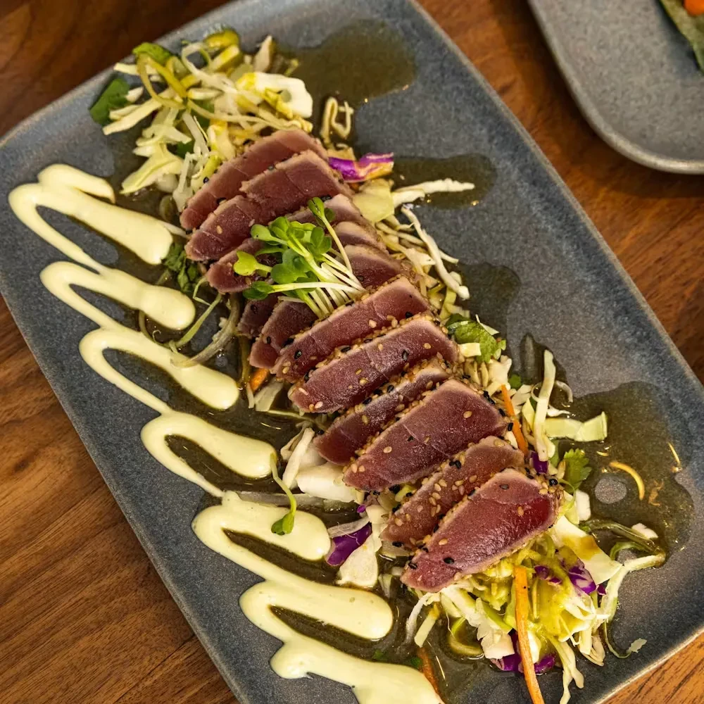 Plated sesame-crusted seared tuna, rare, with vegetables, sauces, and microgreens.