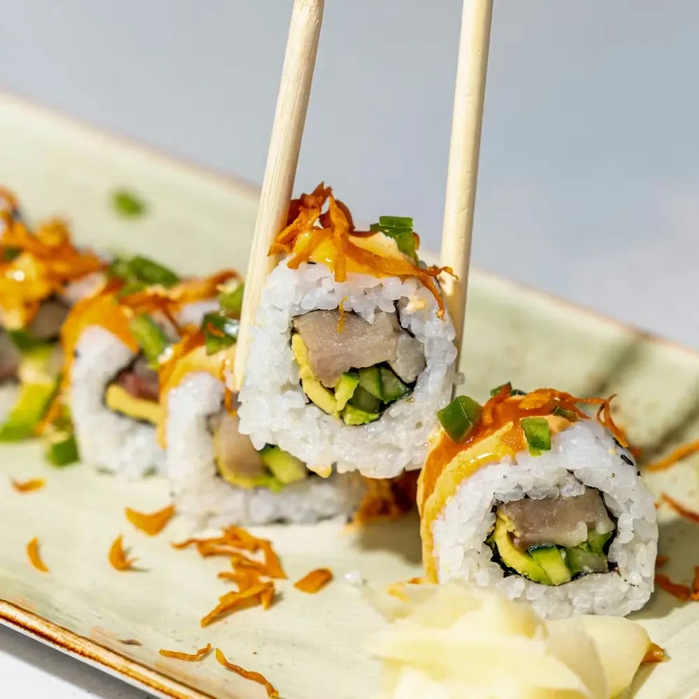 Chopsticks lift one sauce-topped inside-out sushi roll.
