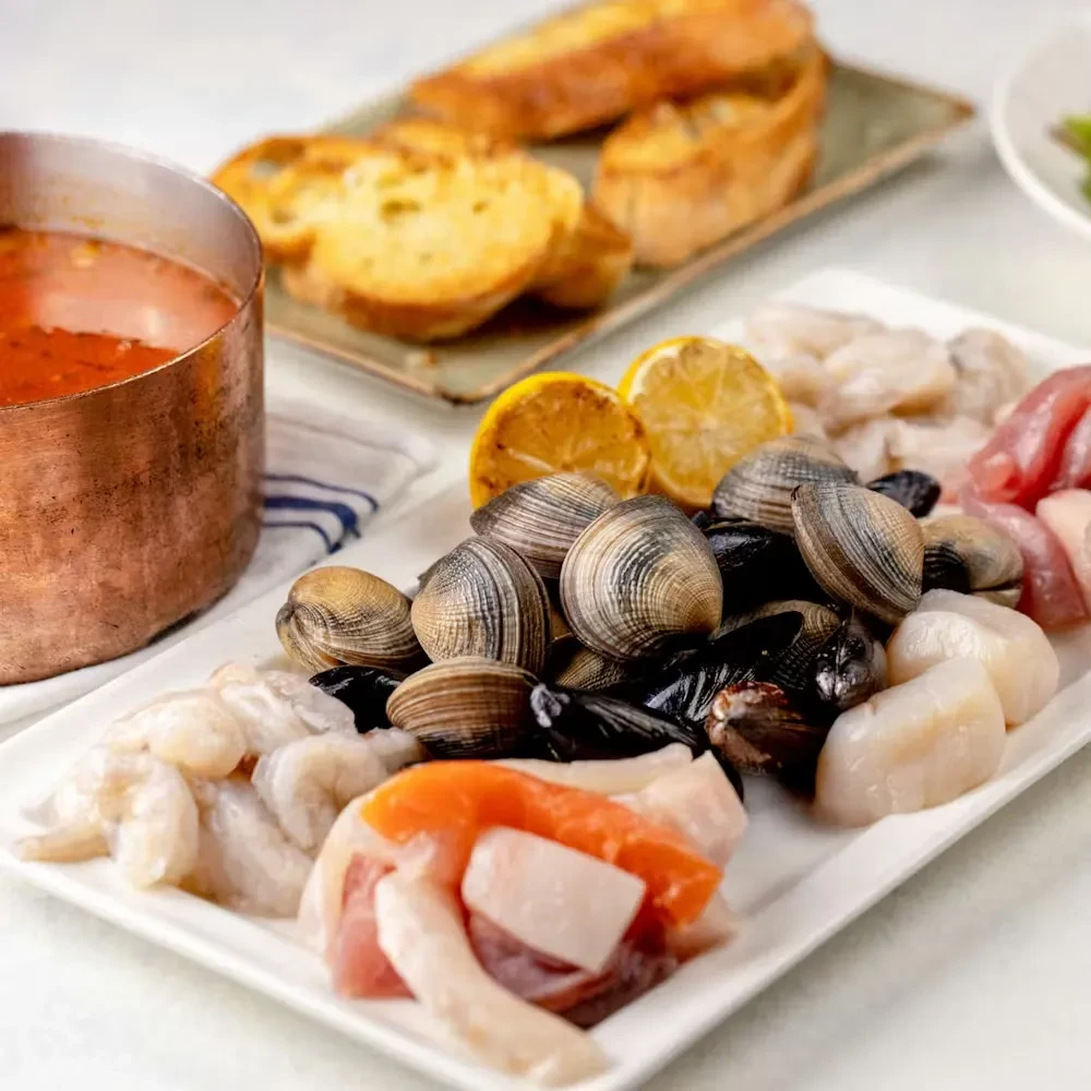 Vibrant raw seafood platter, simmering red sauce, and toasted bread.