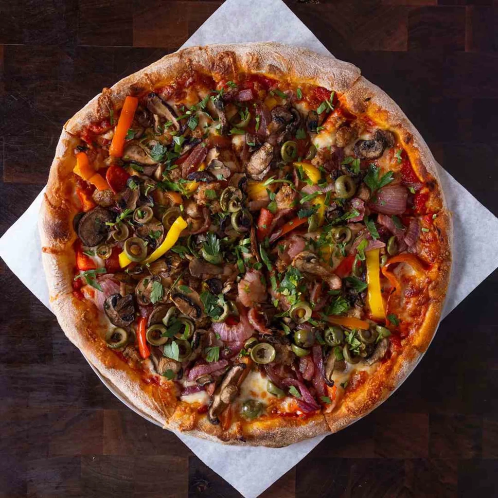 Top-down, freshly baked pizza with mushrooms, olives, peppers, and herbs.