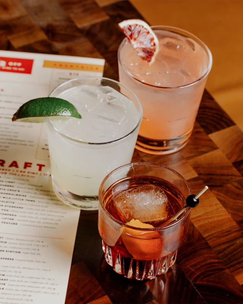 Three diverse cocktails with distinct garnishes on a wooden table.
