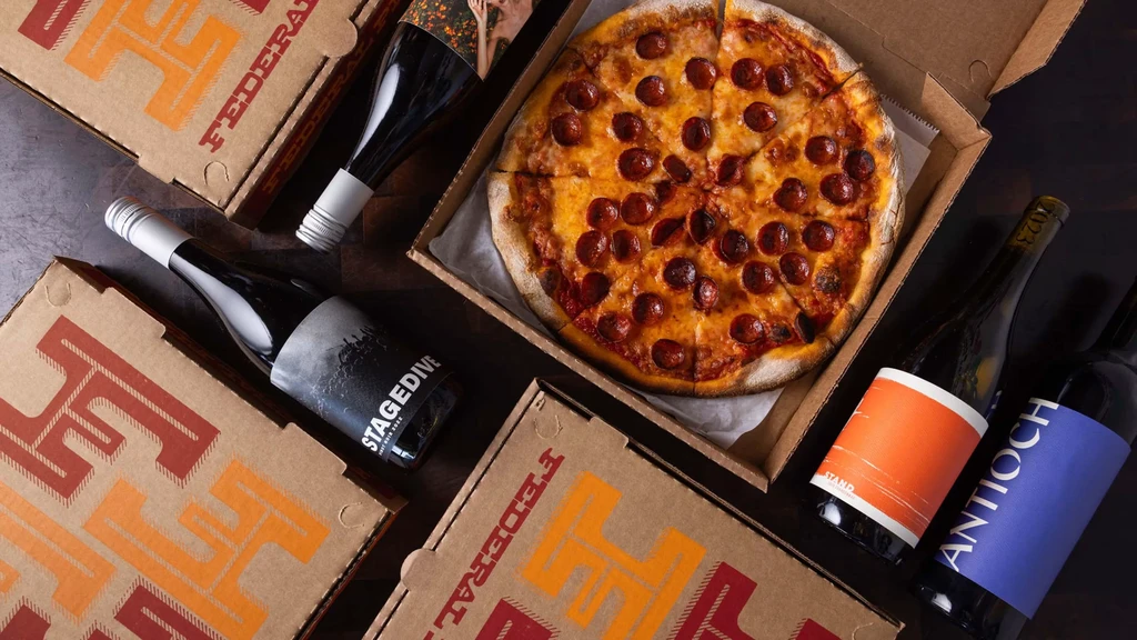 Pepperoni pizza in open box, surrounded by wine and Federal pizza boxes.