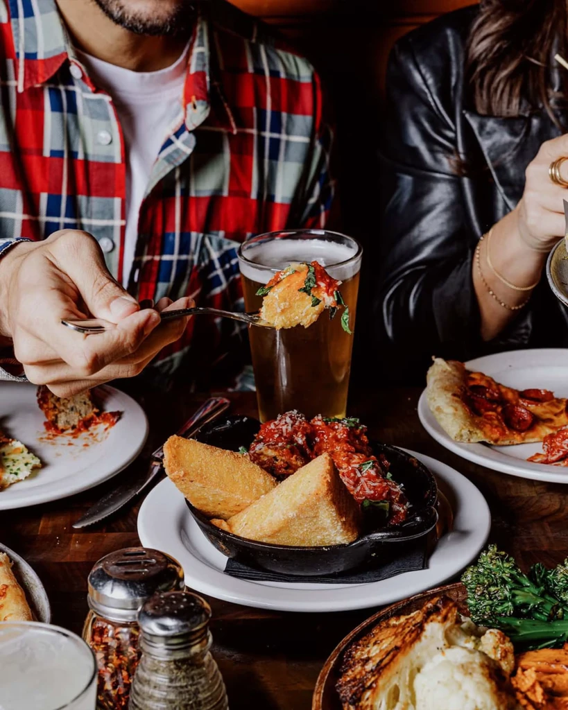 Dining table laden with skillet meatballs, pizza, and roasted vegetables.