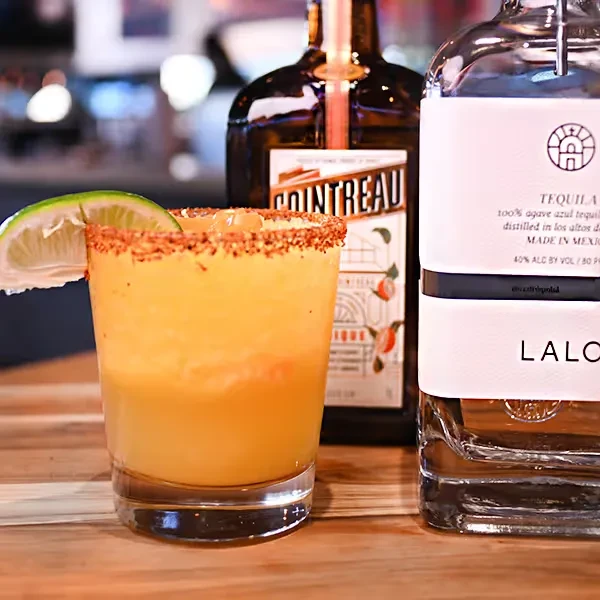 Vibrant orange cocktail with lime, Cointreau and LALO Tequila bottles.