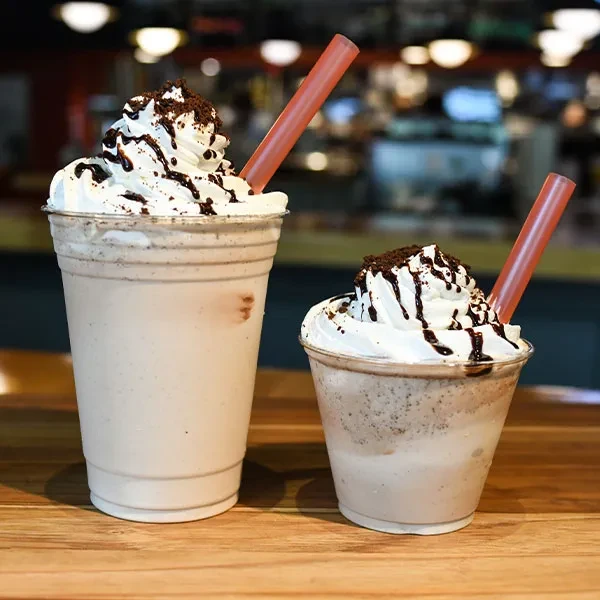 Two milkshakes, different sizes, topped with whipped cream, chocolate, and cookies.