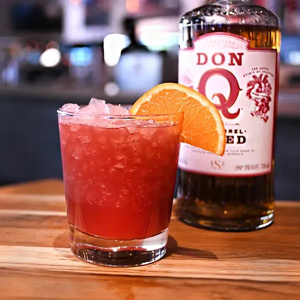 Red cocktail with orange slice and DON Q Barrel RED rum bottle.