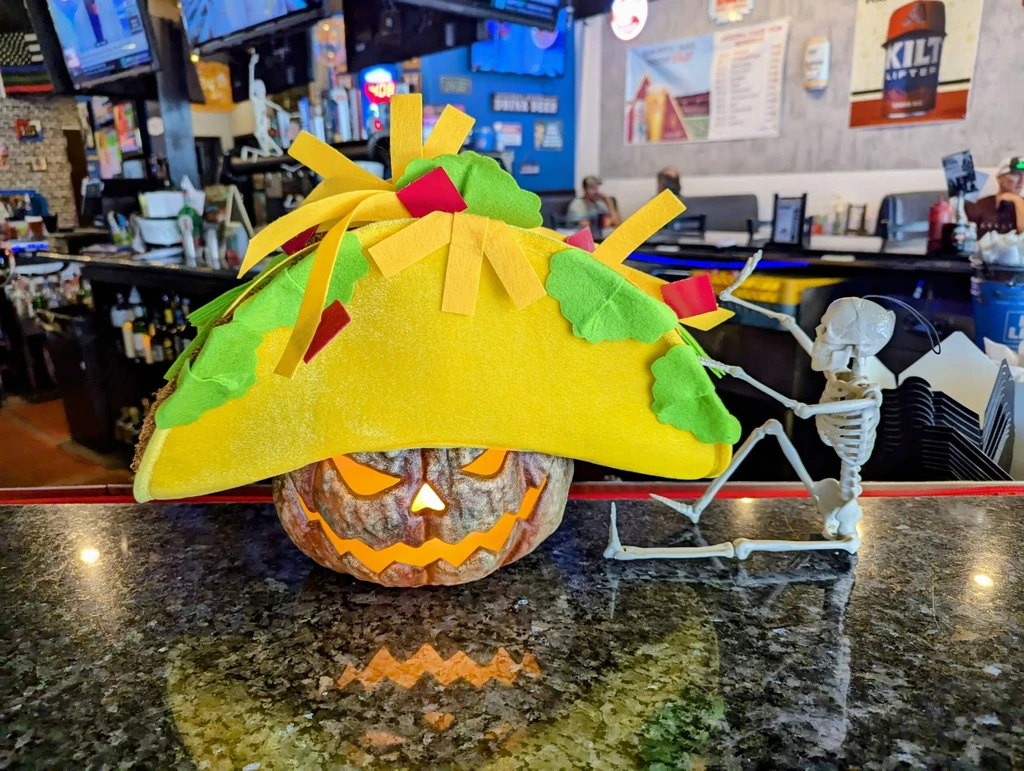 Halloween taco hat, glowing jack-o'-lantern, and skeleton on bar counter.