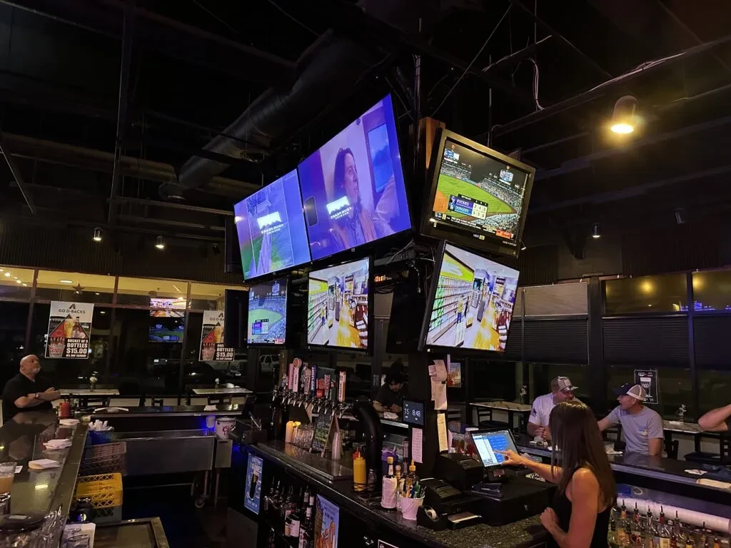 Dimly lit sports bar interior with multiple large TV screens above the bar.