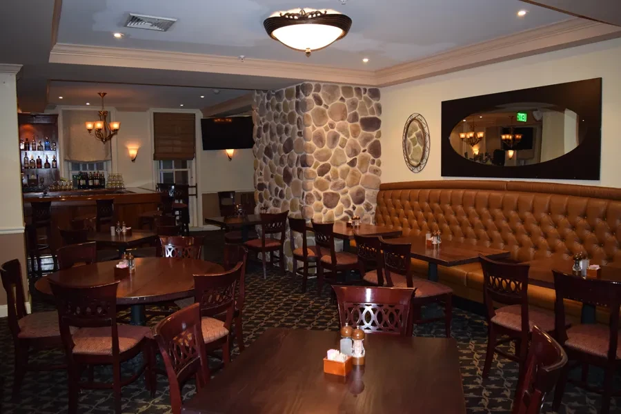 Restaurant dining room with wooden tables, tufted leather banquette, and bar.