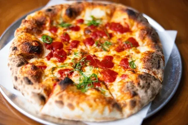 Neapolitan pizza with blistered crust, melted cheese, and fresh green herbs.