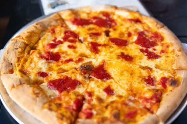 A whole cheese pizza, pre-cut, with bubbly cheese and red sauce.
