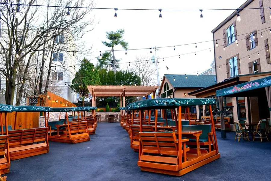 Outdoor restaurant patio with swing-bench units, green canopies, bistro lights.