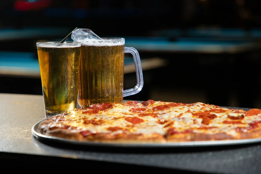 Pepperoni pizza and two glasses of beer on a metal tray.