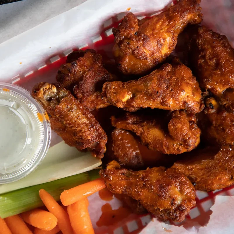 Sauce-coated fried chicken wings, dipping sauce, carrots, and celery sticks.